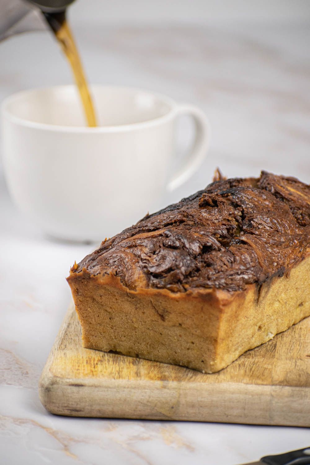 Nutella banana bread on a wooden cutting board with coffee being poured in the background.