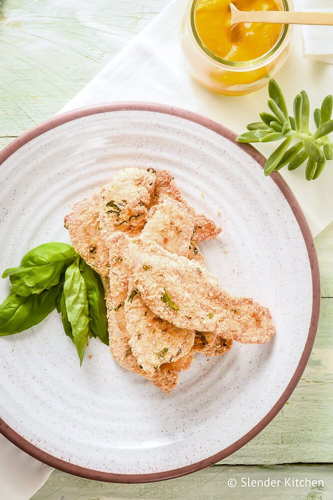 Parmesan chicken on a white plate with basil and a small jar of mustard.
