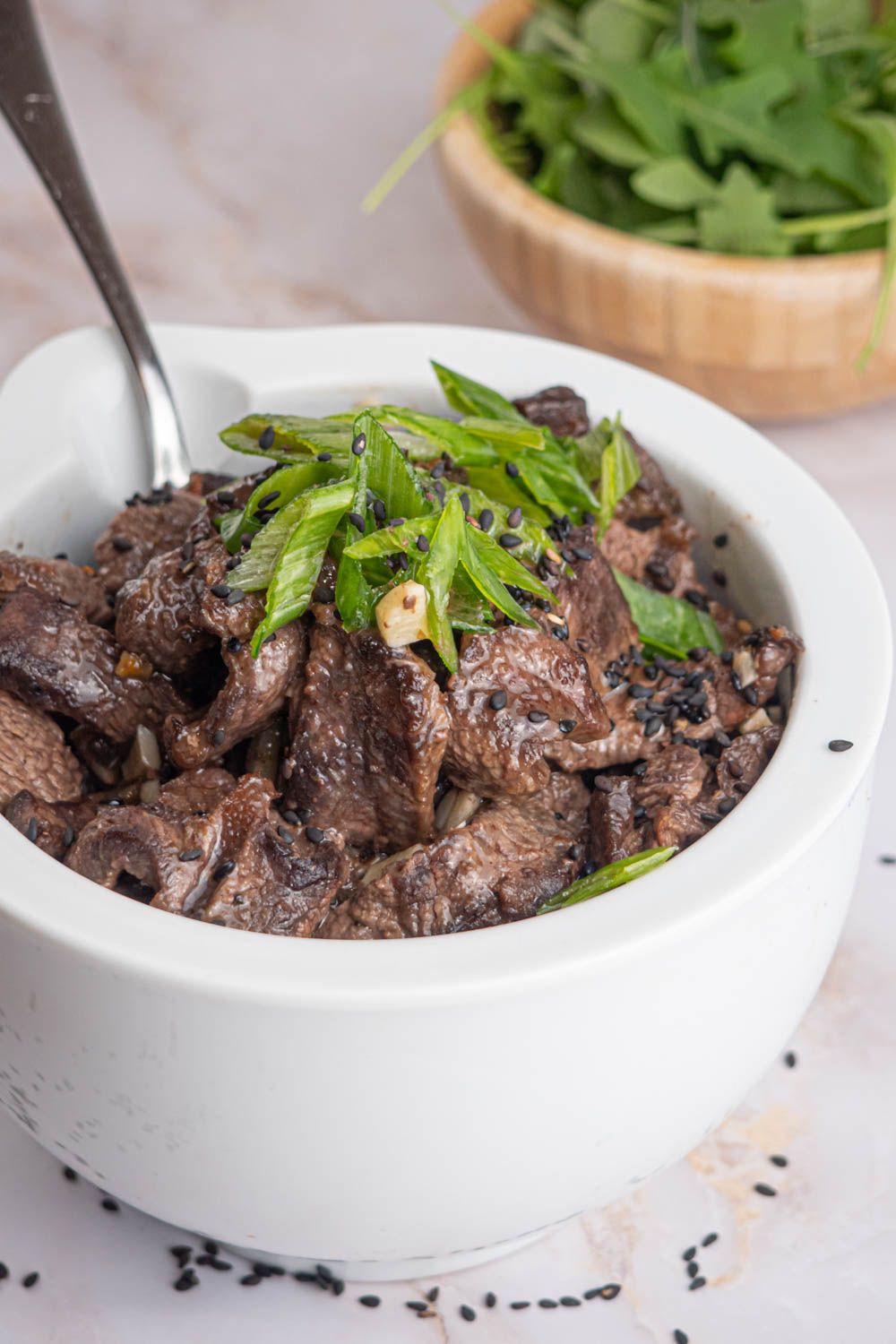 Sesame beef with black sesame seeds and green onions in a bowl.