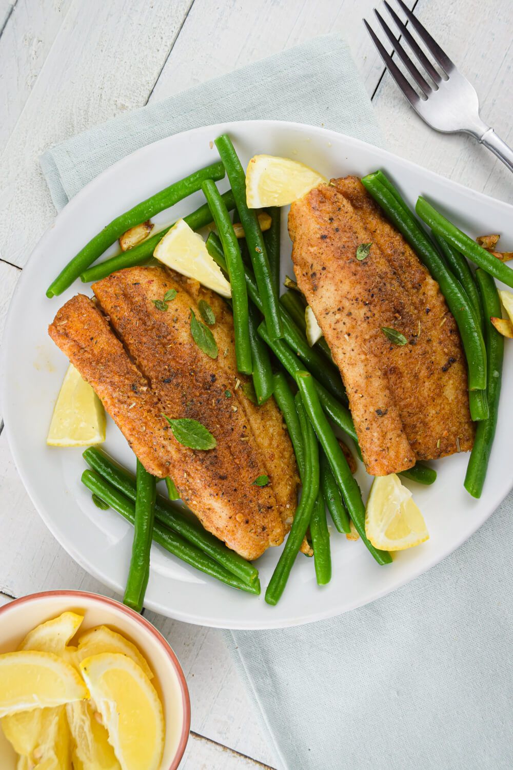 Tilapia pan seared with a spice rub and green beans on a plate with lemon on the side.