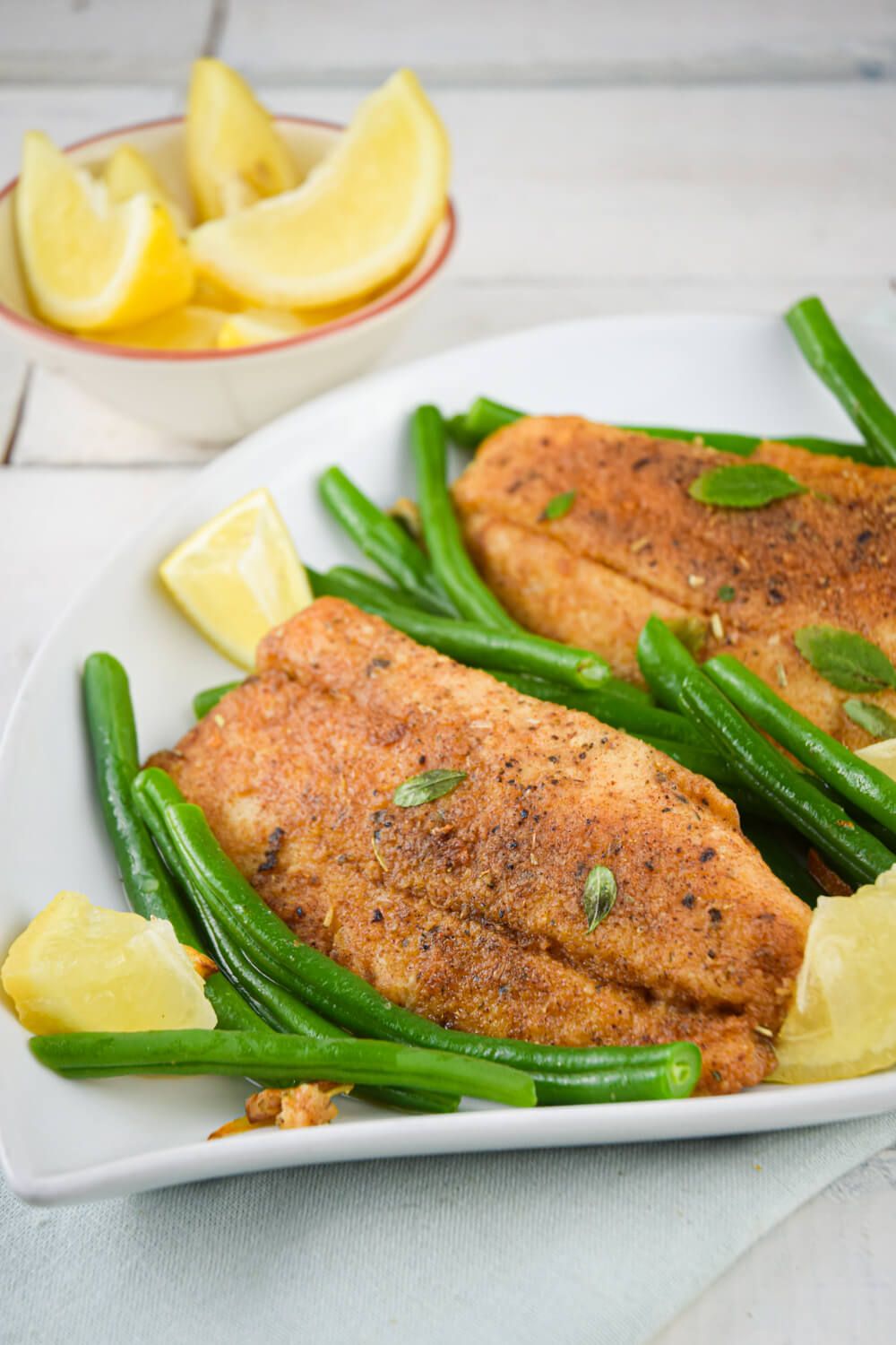 Seared tilapia with green beans and lemon on a plate.
