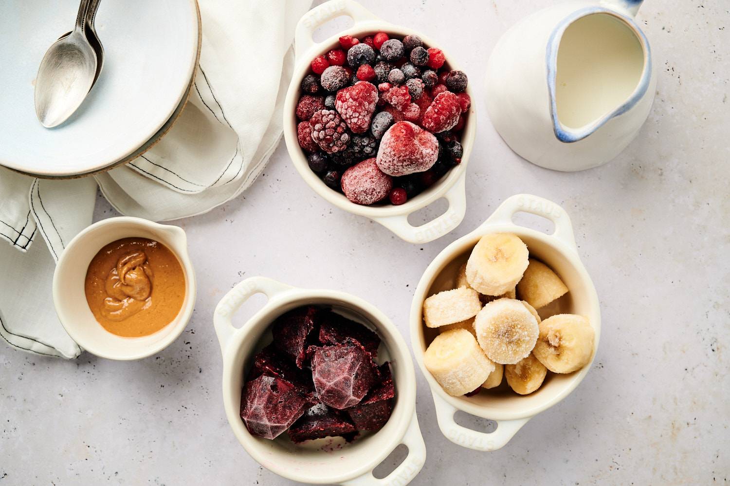 "Acai bowl ingredients in small bowls, including frozen berries, bananas, acai puree, peanut butter, and milk.