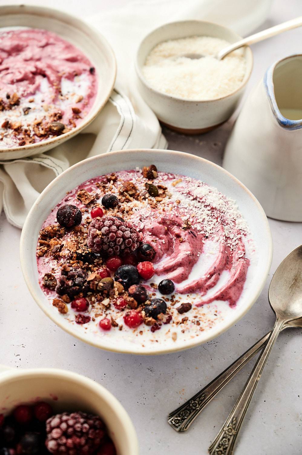 Acai bowl topped with frozen berries, granola, and coconut flakes, with a swirl of yogurt and milk in a ceramic bowl.