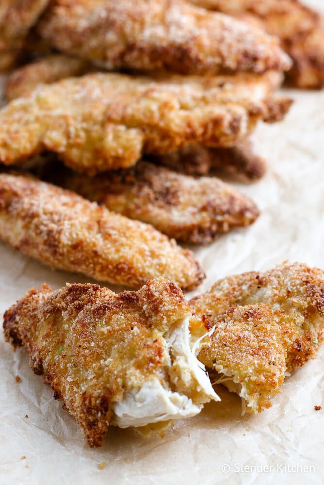 Breaded chicken tenders made in the air fryer on a cutting board with one chicken strip cut in half.