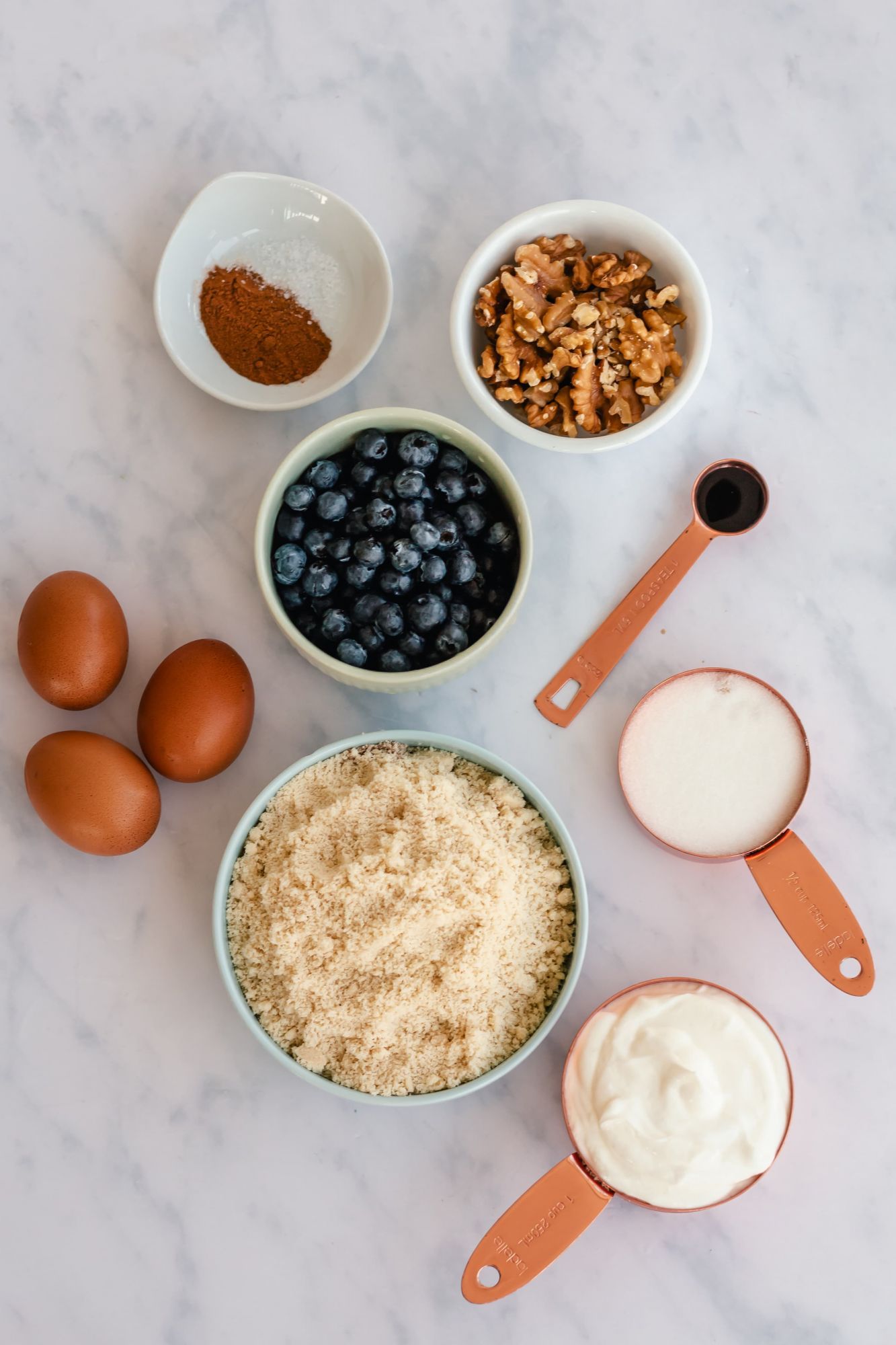 Ingredients for almond flour blueberry muffins including almond flour, blueberries, eggs, yogurt, walnuts, and cinnamon.