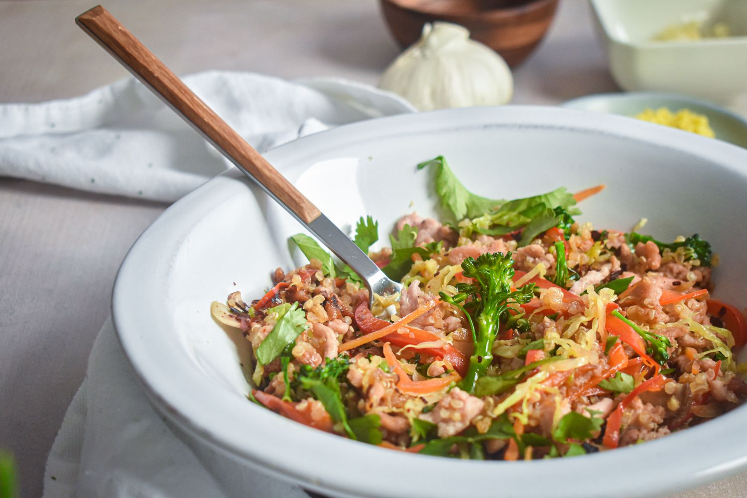 Asian ground turkey and vegetable stir fry with quinoa in a bowl with a wooden fork.