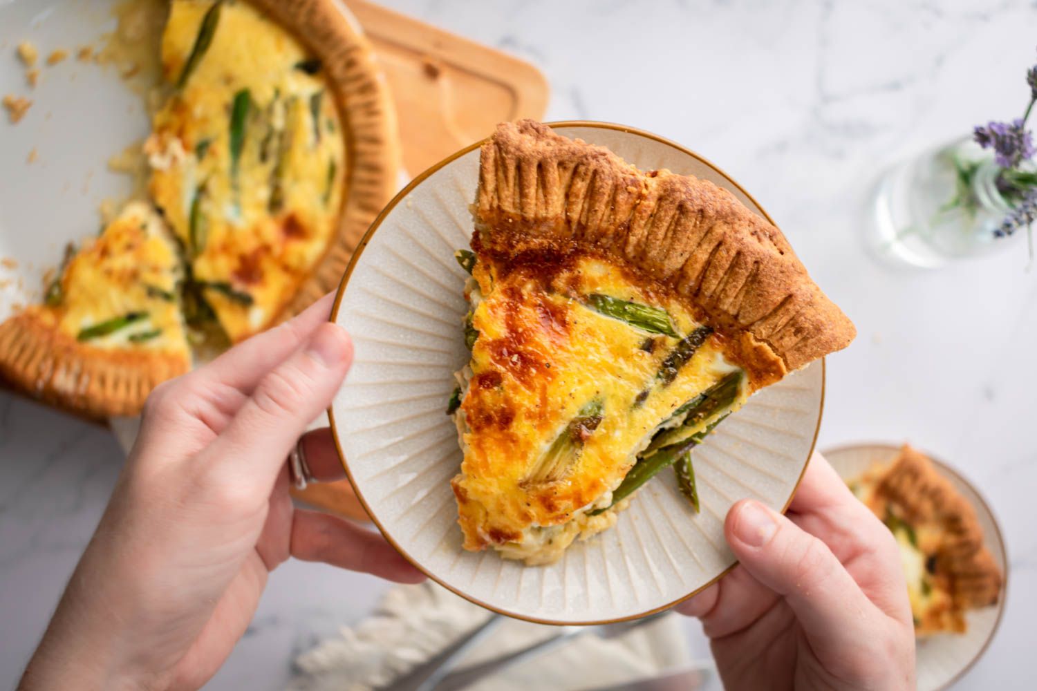 Slice of asparagus quiche served on a plate and spears of asparagus, onion, and cheese.