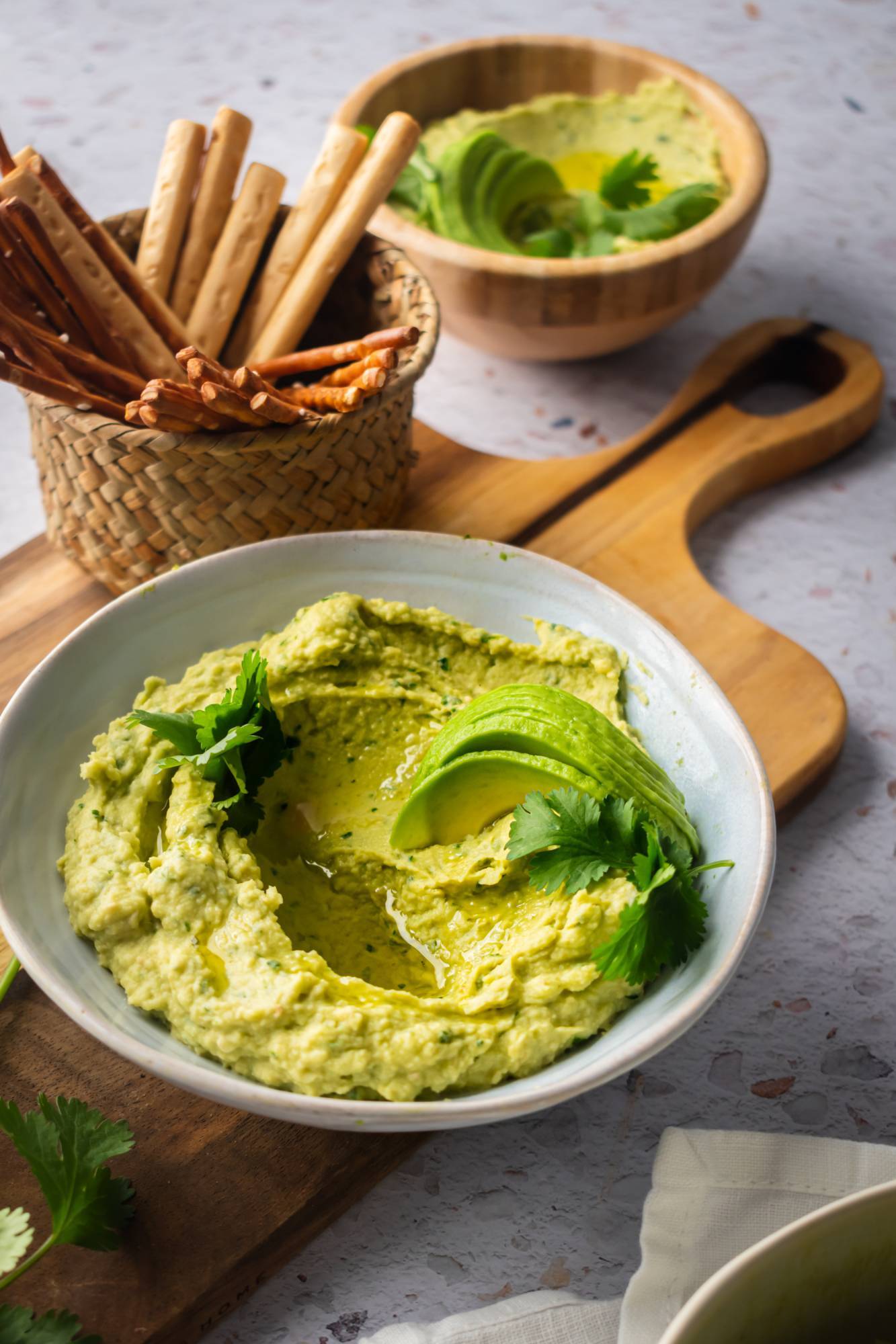 Avocado cilantro hummus with breadsticks and pretzels served with fresh sliced avocado.