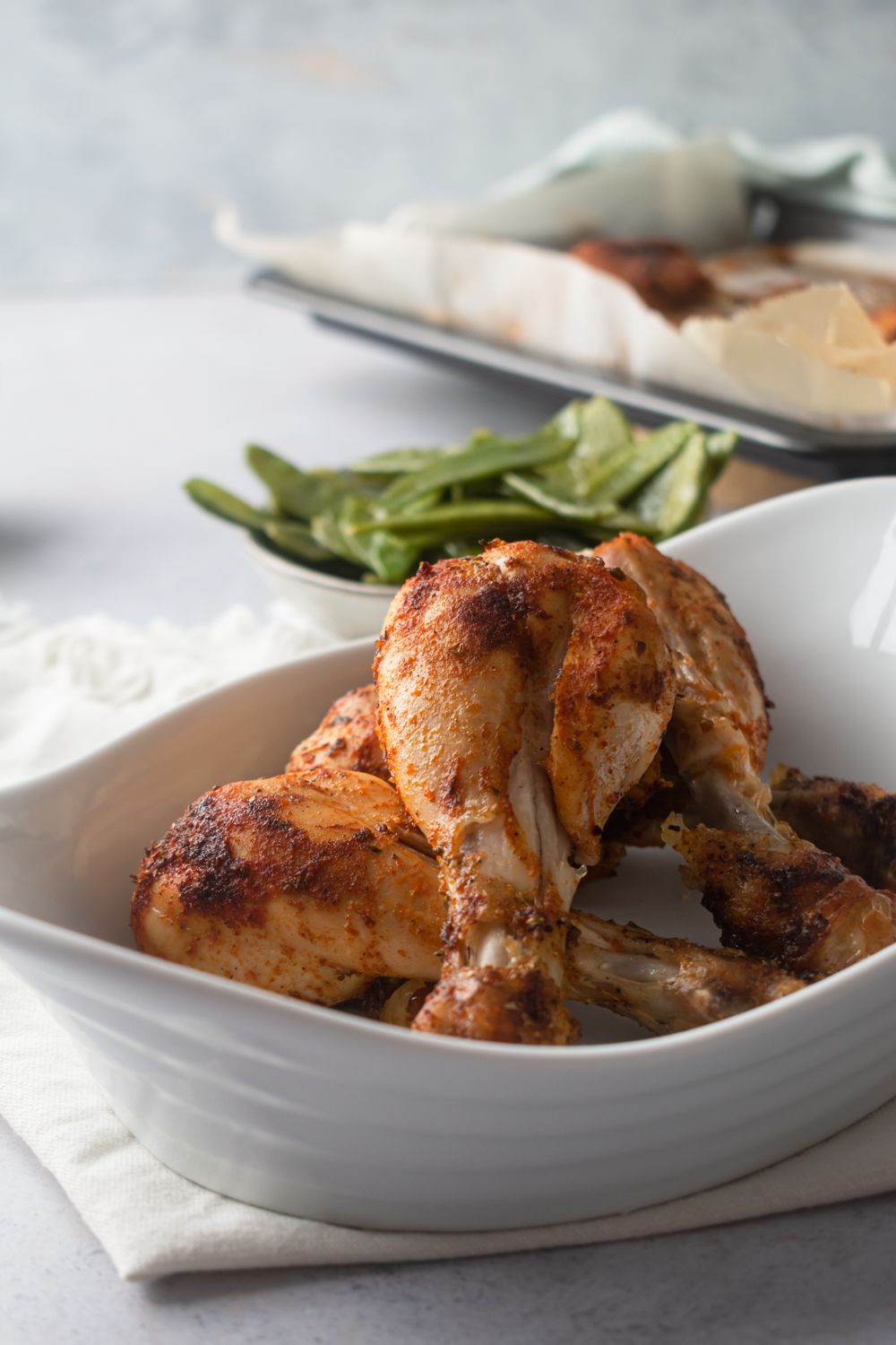 Chicken drumsticks baked in the oven with spices and served in a plate with snow peas on the side.
