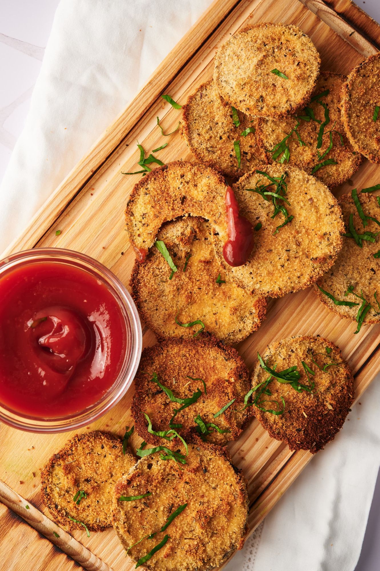 Eggplant cutlets with breading on a cutting board with tomato sauce for dipping.