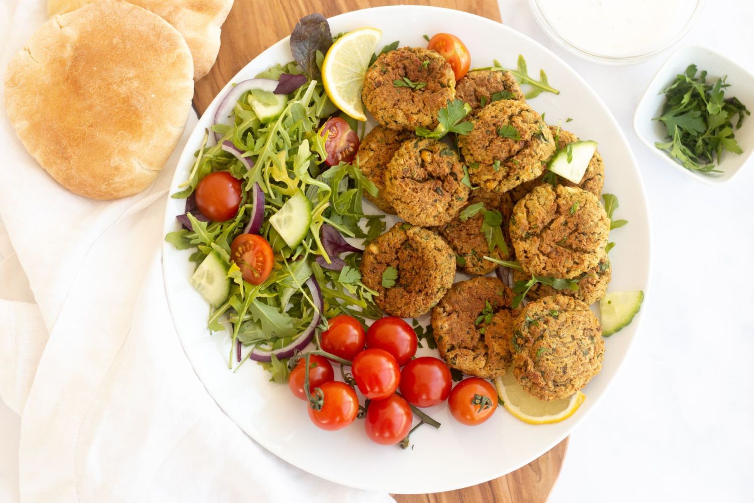 Chickpea falafel that are baked with crispy edges on a plate with lettuce, tomatoes, and cucumbers.