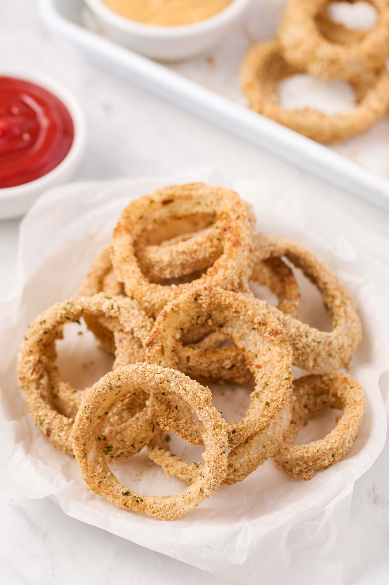 Crispy baked onion rings on a plate served with ketchup.