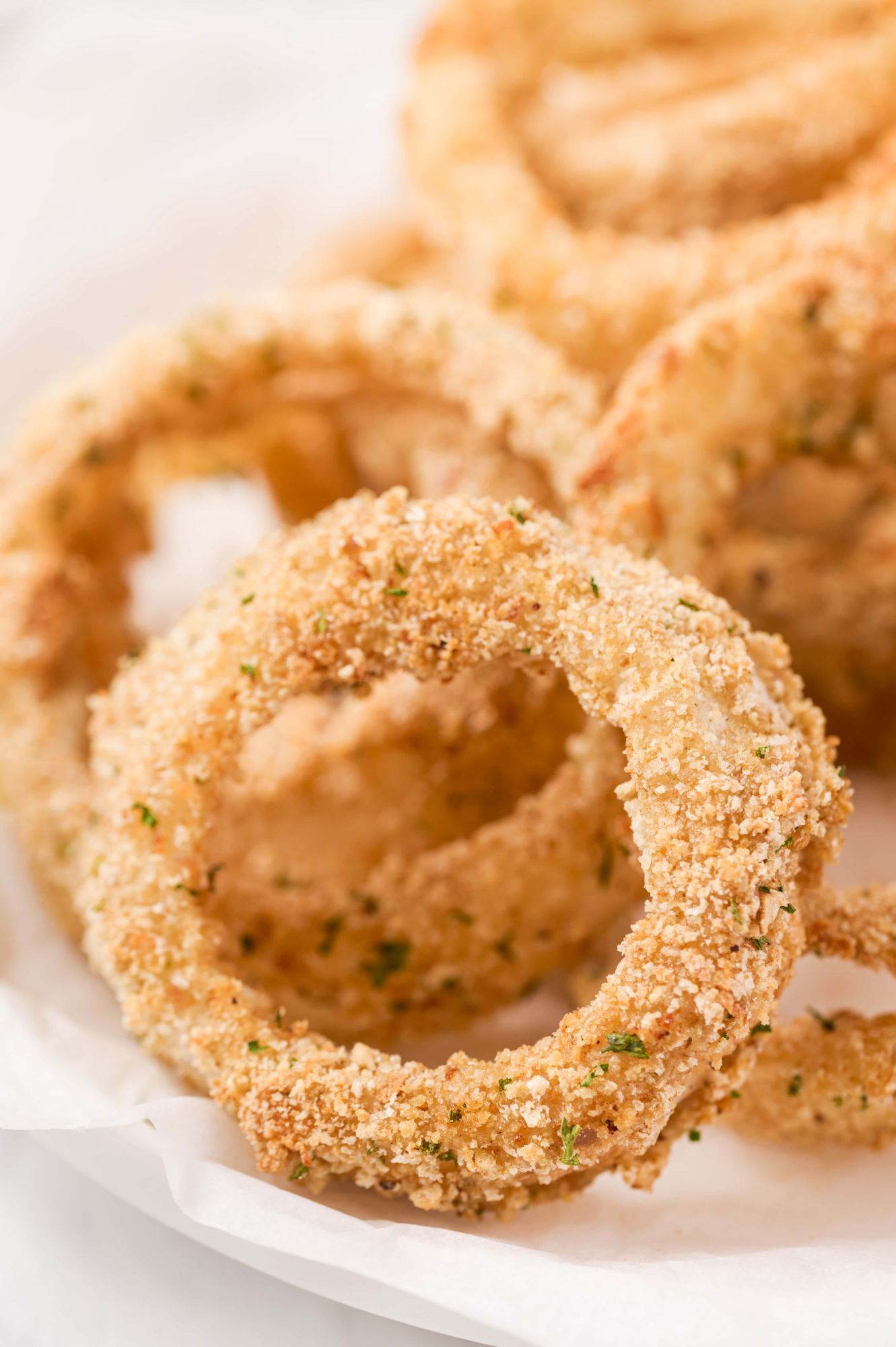 Homemade onion rings baked with breadcrumbs on a plate with herbs and seasoned salt.