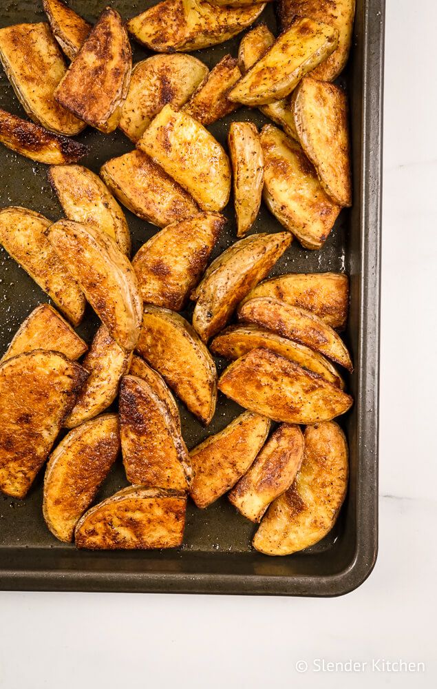 Baked potato wedges with a crispy exterior on a baking sheet.