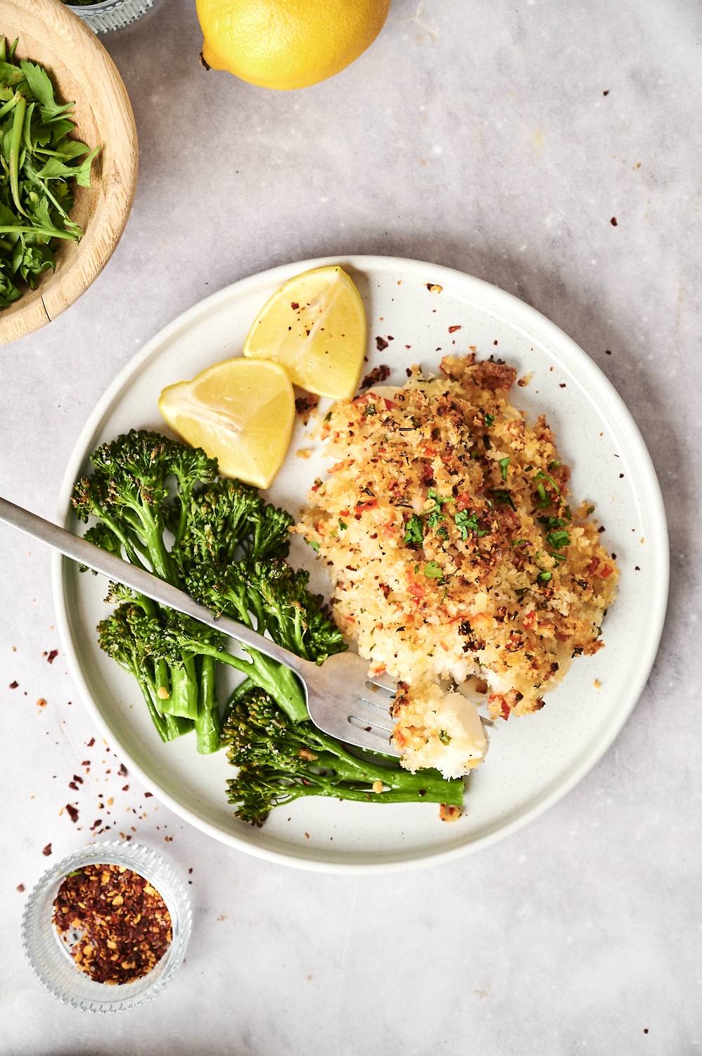 Stuffed haddock with seafood stuffing, broccoli, and lemon on a plate with a fork.