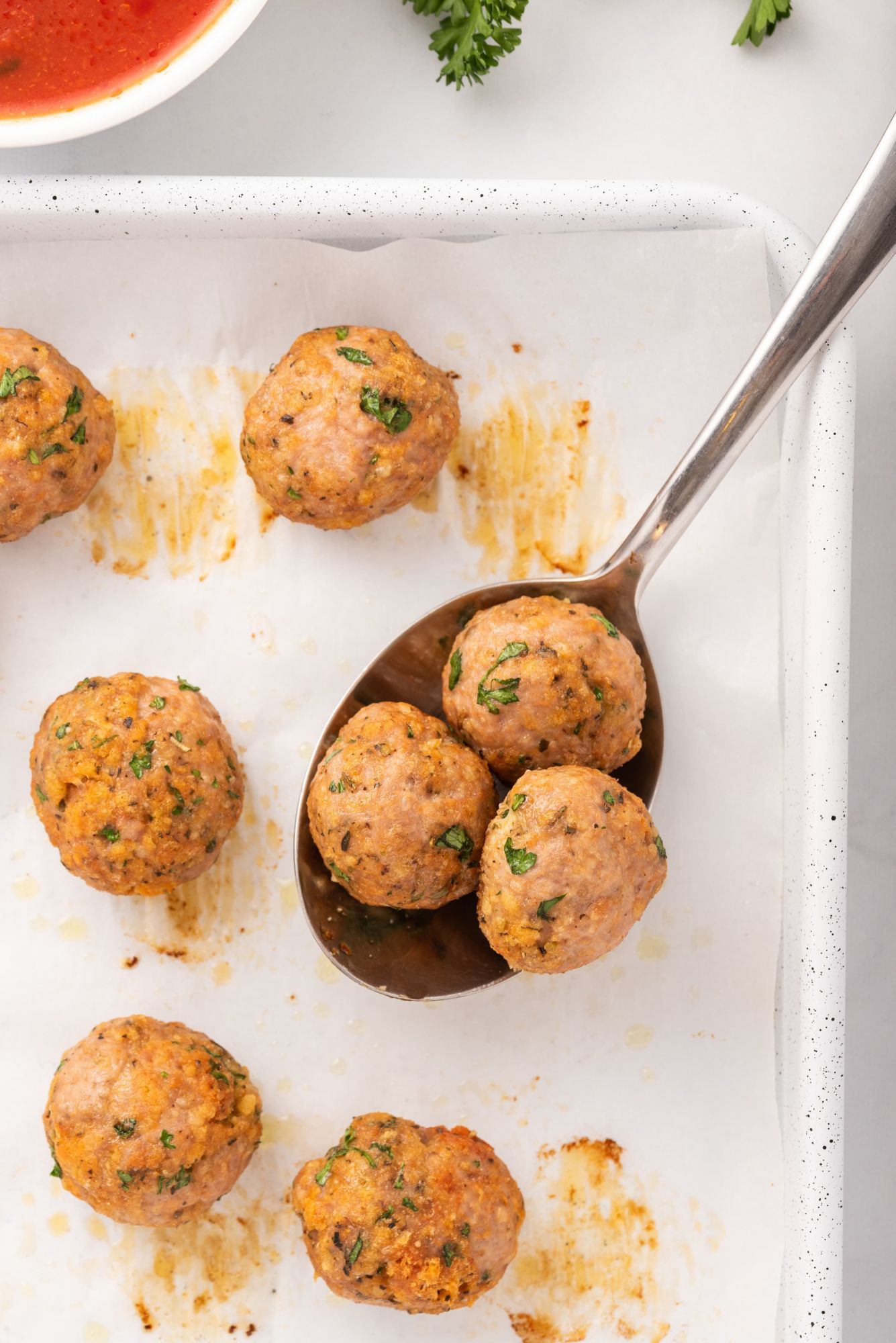 Ground turkey meatballs with parsley and Parmesan on a metal spoon.