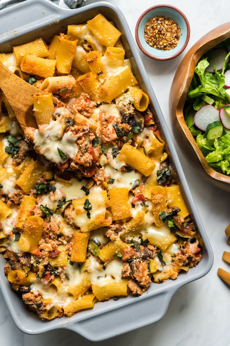 Turkey and vegetable baked ziti in a casserole dish with melted cheese and fresh basil.