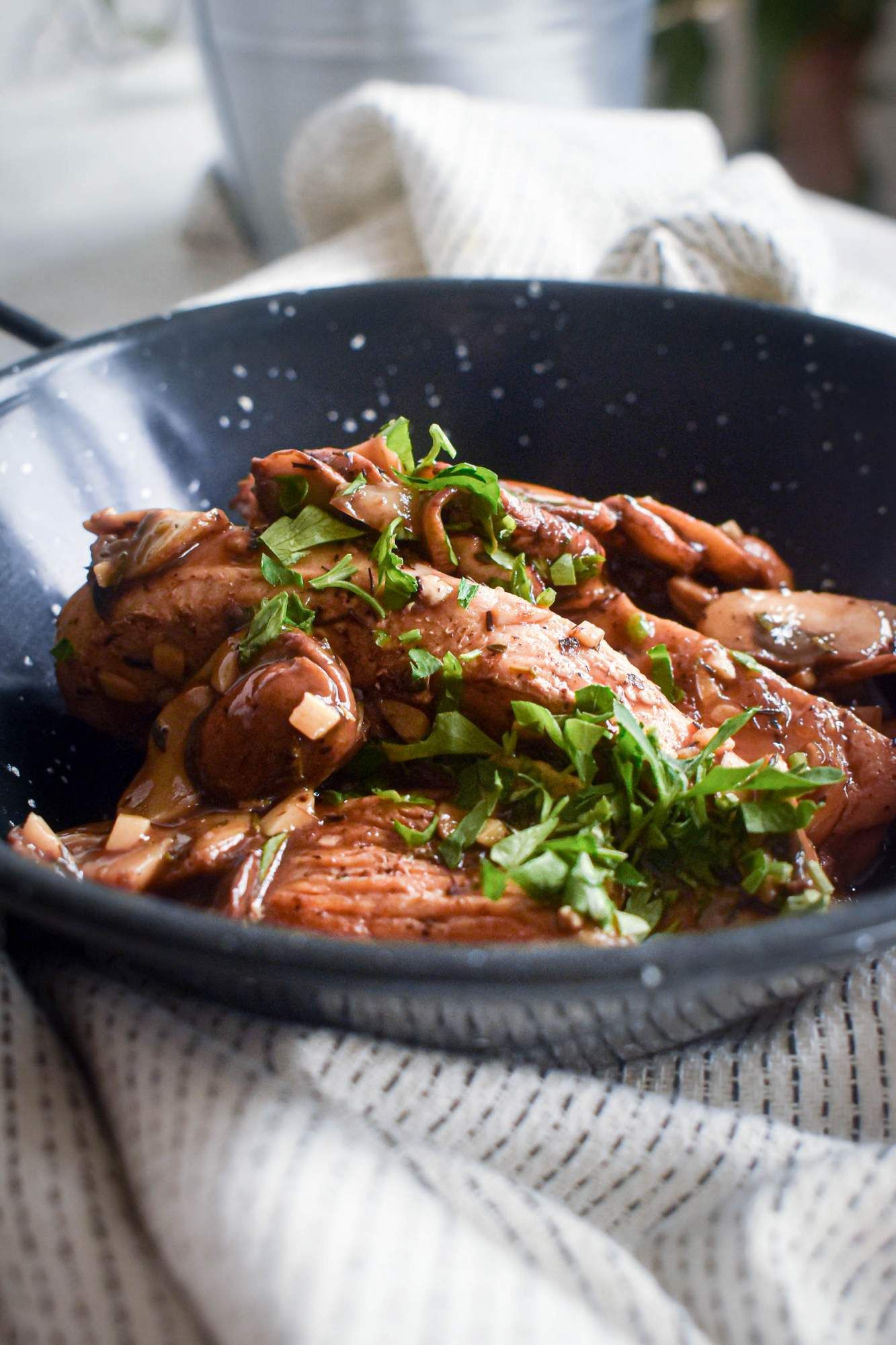 Chicken with balsamic vinegar sauce and mushrooms in a blue bowl with fresh parsley.