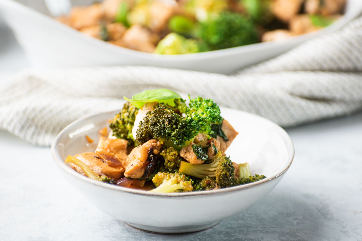 Chicken and broccoli stir fry with fresh basil, lemon, and soy sauce served in a white bowl.