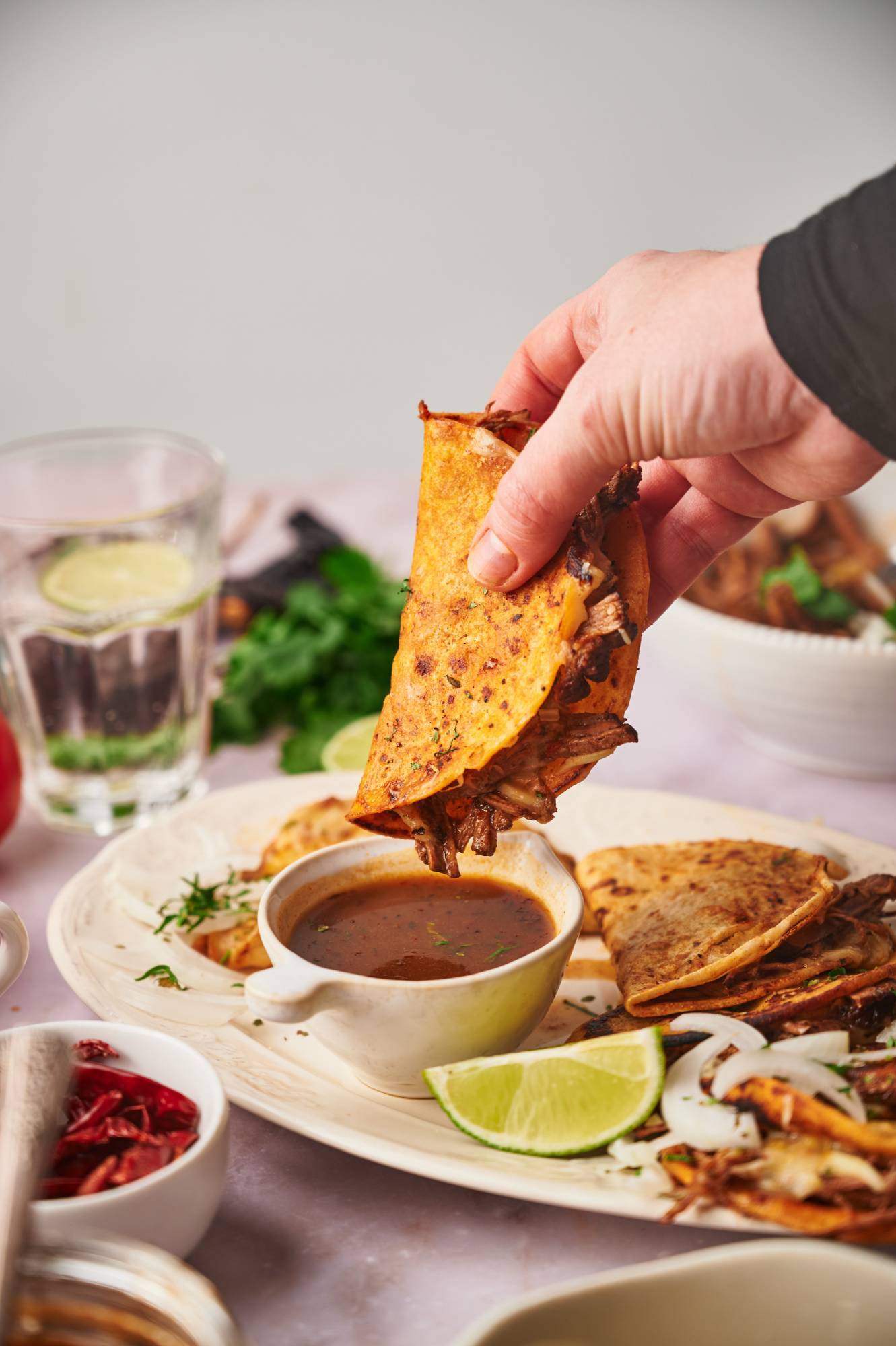 Birria taco being dipped in a bowl of consome with cilantro, onion, and lime.
