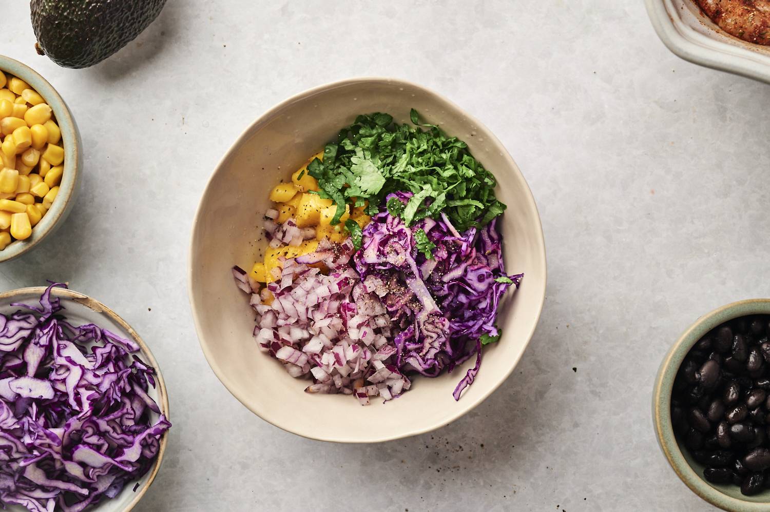 Bowl filled with fresh ingredients including diced mango, red onion, purple cabbage, and chopped cilantro, ready for assembling blackened shrimp bowls.