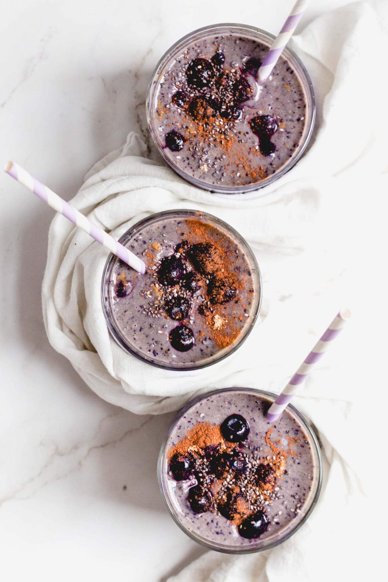 Banana blueberry smoothie in three glasses with fresh blueberries and cinnamon on top.
