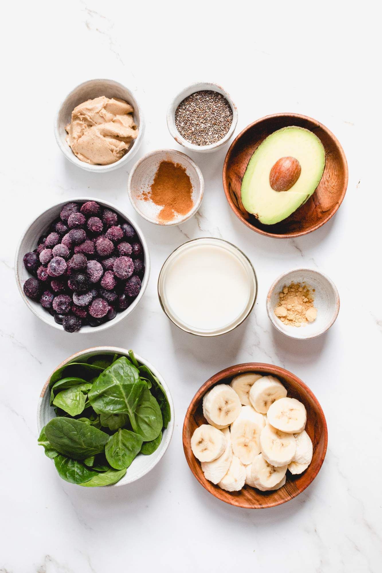 Ingredients for a banana and blueberry smoothie including sliced bananas, almond milk, frozen blueberries, avocado, cinnamon, and more.