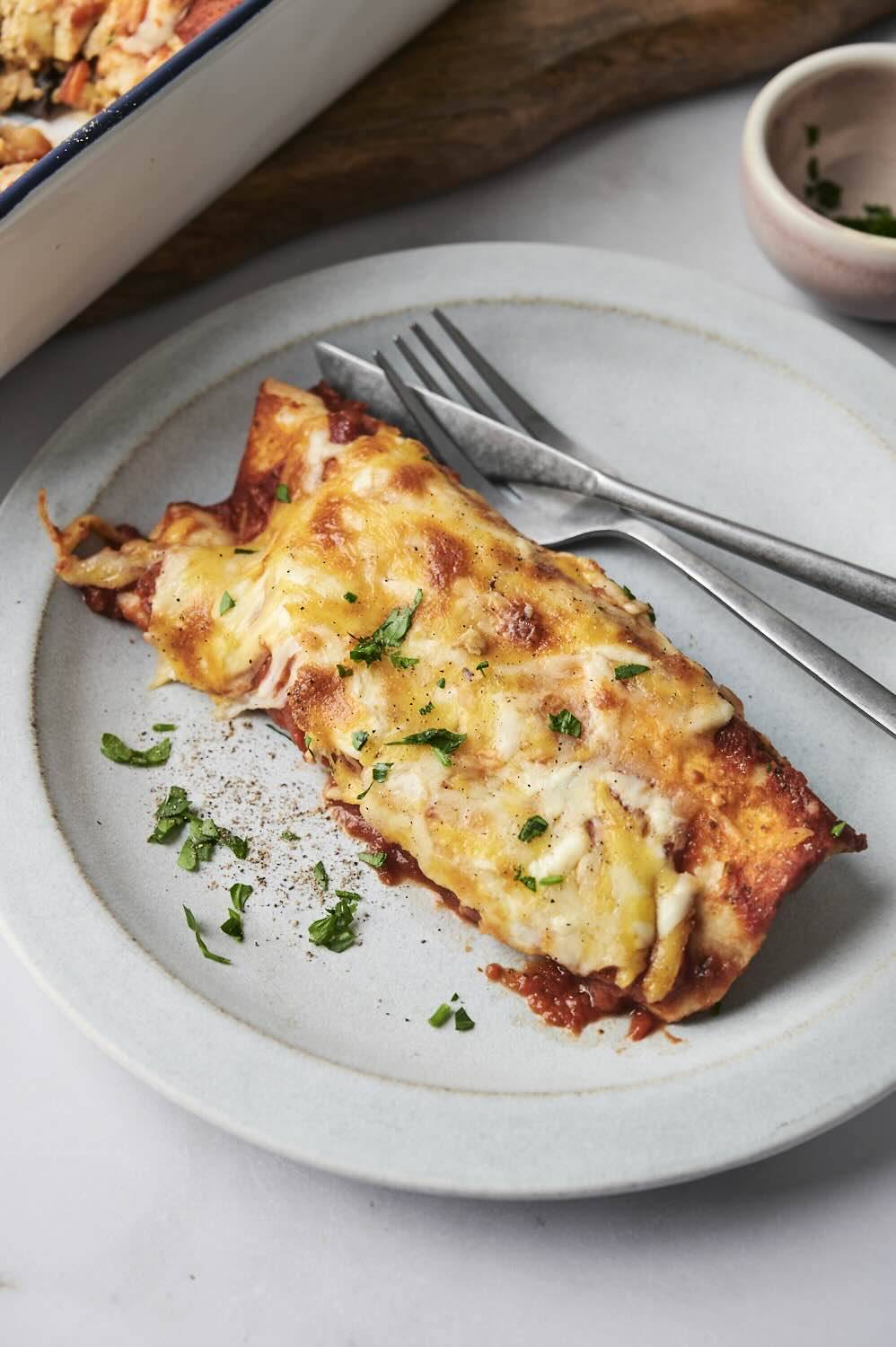 A serving of baked breakfast enchiladas, topped with melted cheese and garnished with fresh herbs on a plate.