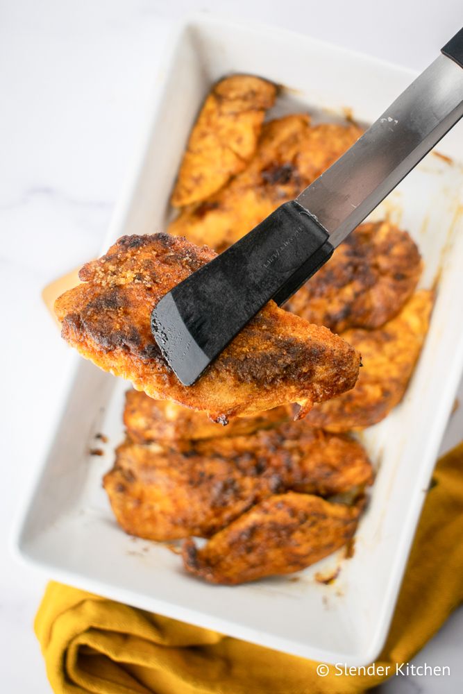 Brown sugar chicken being held up with tongs with a crispy coating.