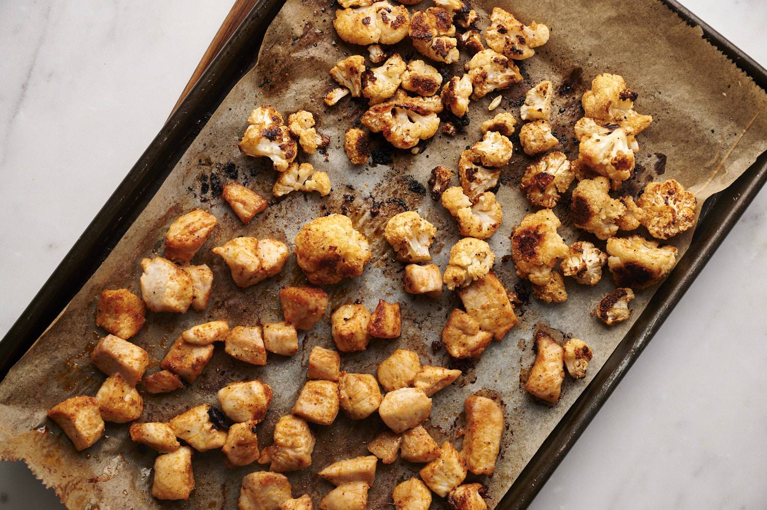 Buffalo chicken and cauliflower on a sheet pan with parchment paper. 