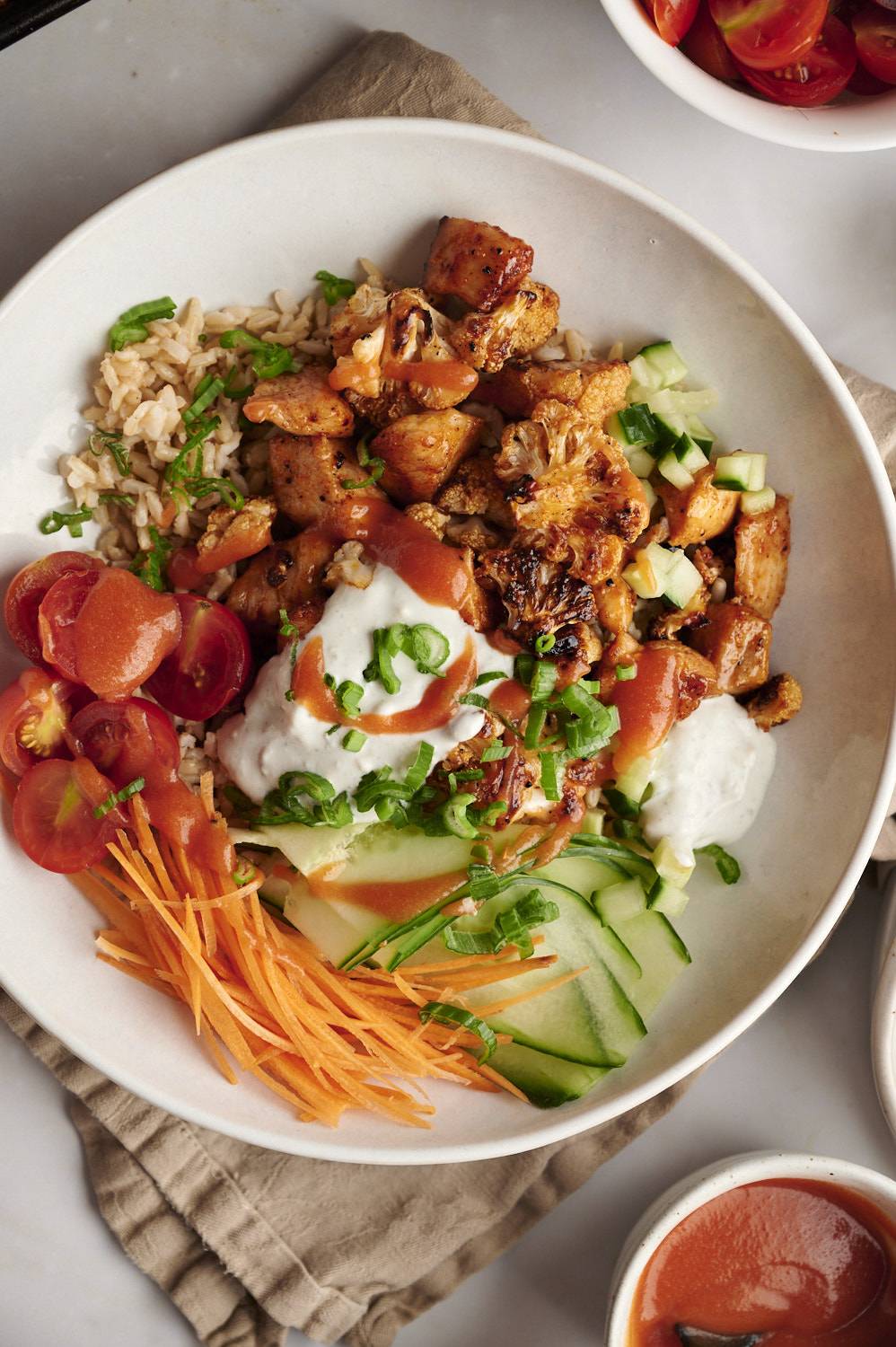 Buffalo chicken rice bowls with cauliflower, carrots, cucumber, tomatoes, buffalo sauce, and blue cheese.