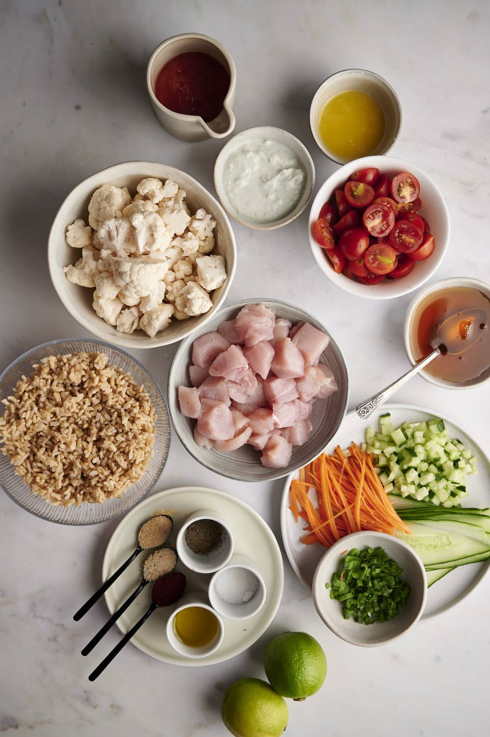 Ingredients for buffalo chicken bowls including chicken breast, rice, buffalo sauce, cauliflower, spices, and vegetables. 