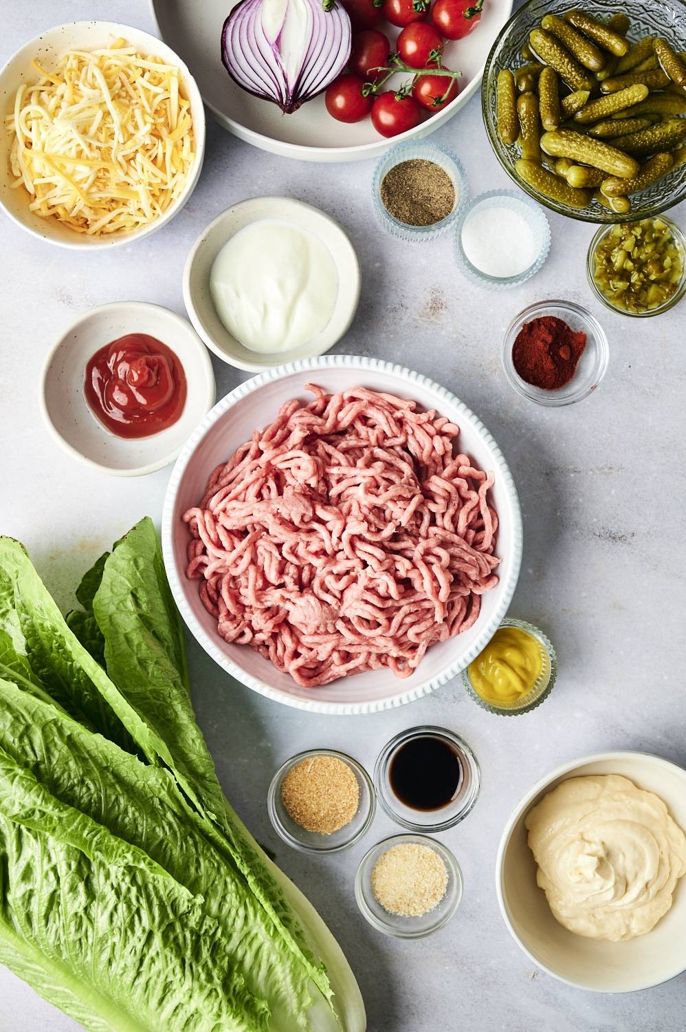Ingredients for burger bowls including ground beef, cheese, lettuce, seasoning, pickles, tomatoes, and red onion.