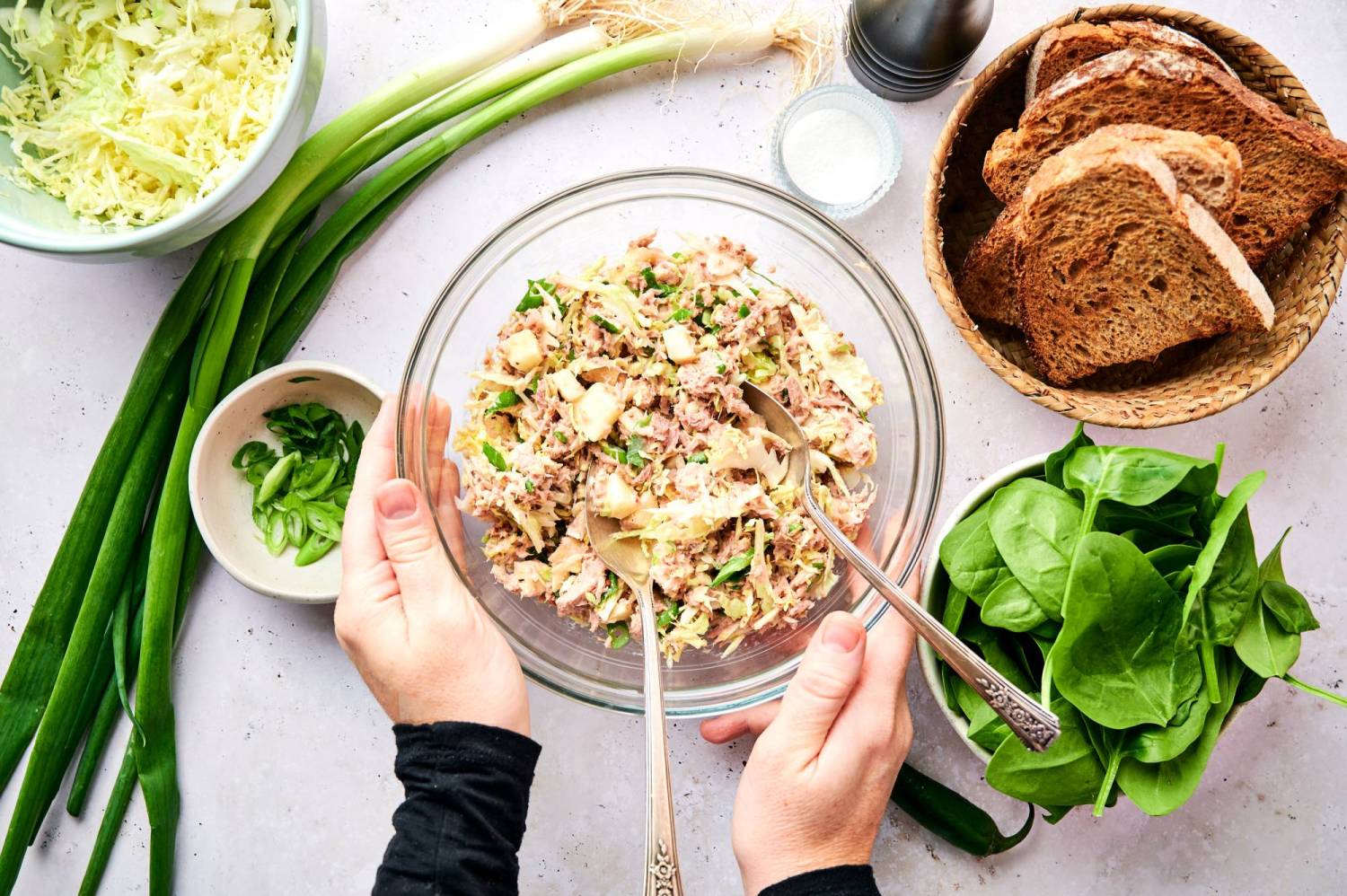 Tuna and cabbage salad in a glass bowl wiht green onions, spinach, and whole grain bread on the side.