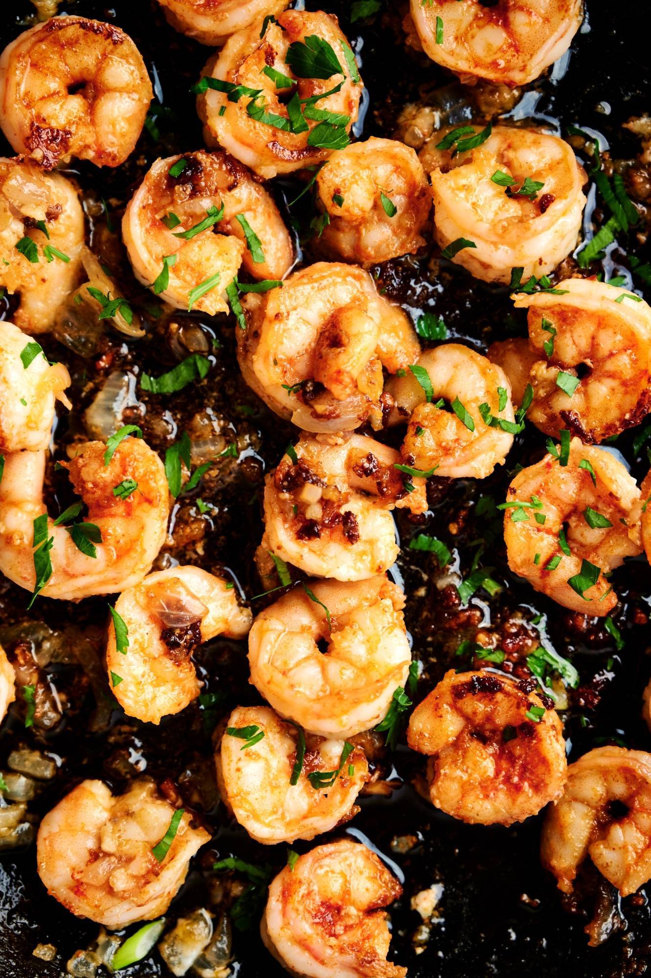 Mexican garlic shrimp cooking in a cast iron skillet with garlic, parsley, butter, and onion.