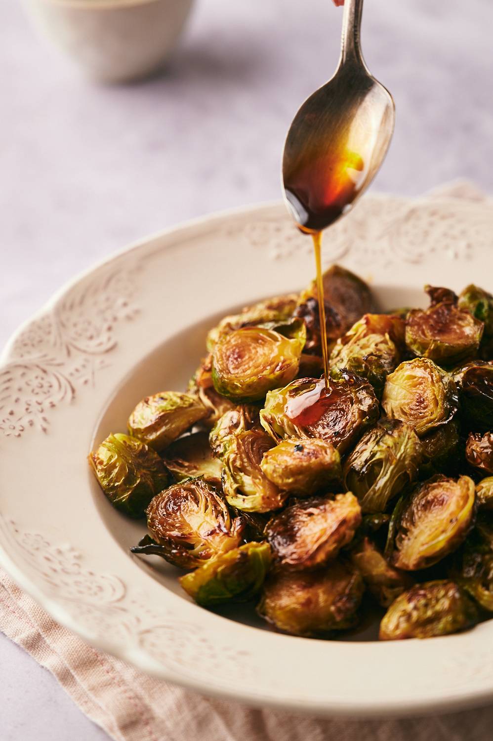 Crispy caramelized Brussels sprouts in a bowl with balsamic glaze being drizzled on top.