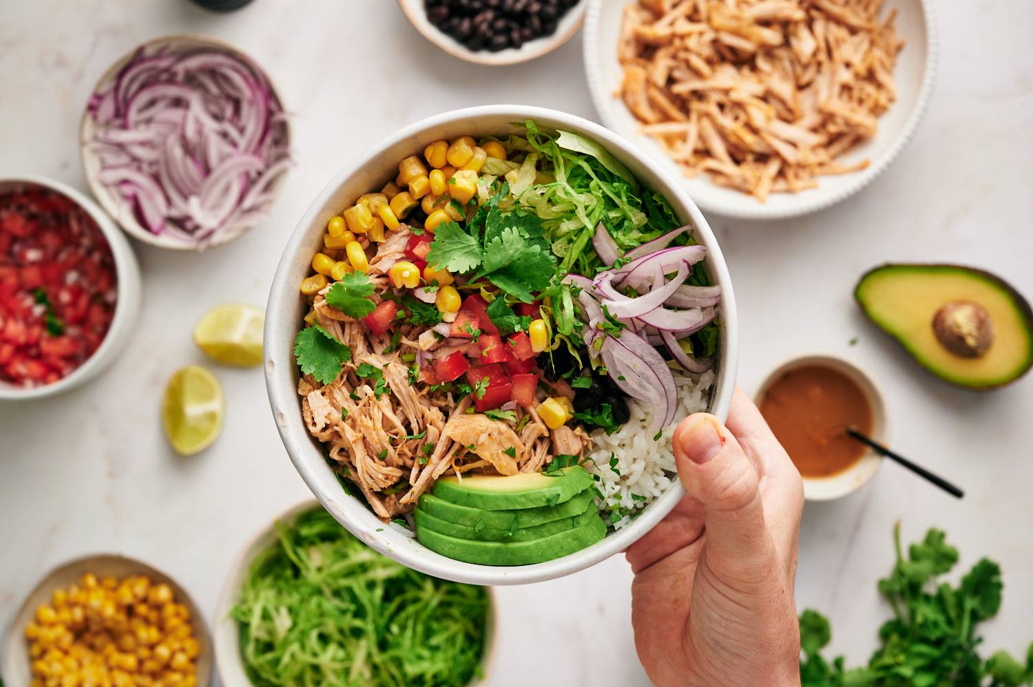 Carnitas taco bowls with cilantro rice, avocado, pico de gallo, corn, and black beans with extra toppings on the side.