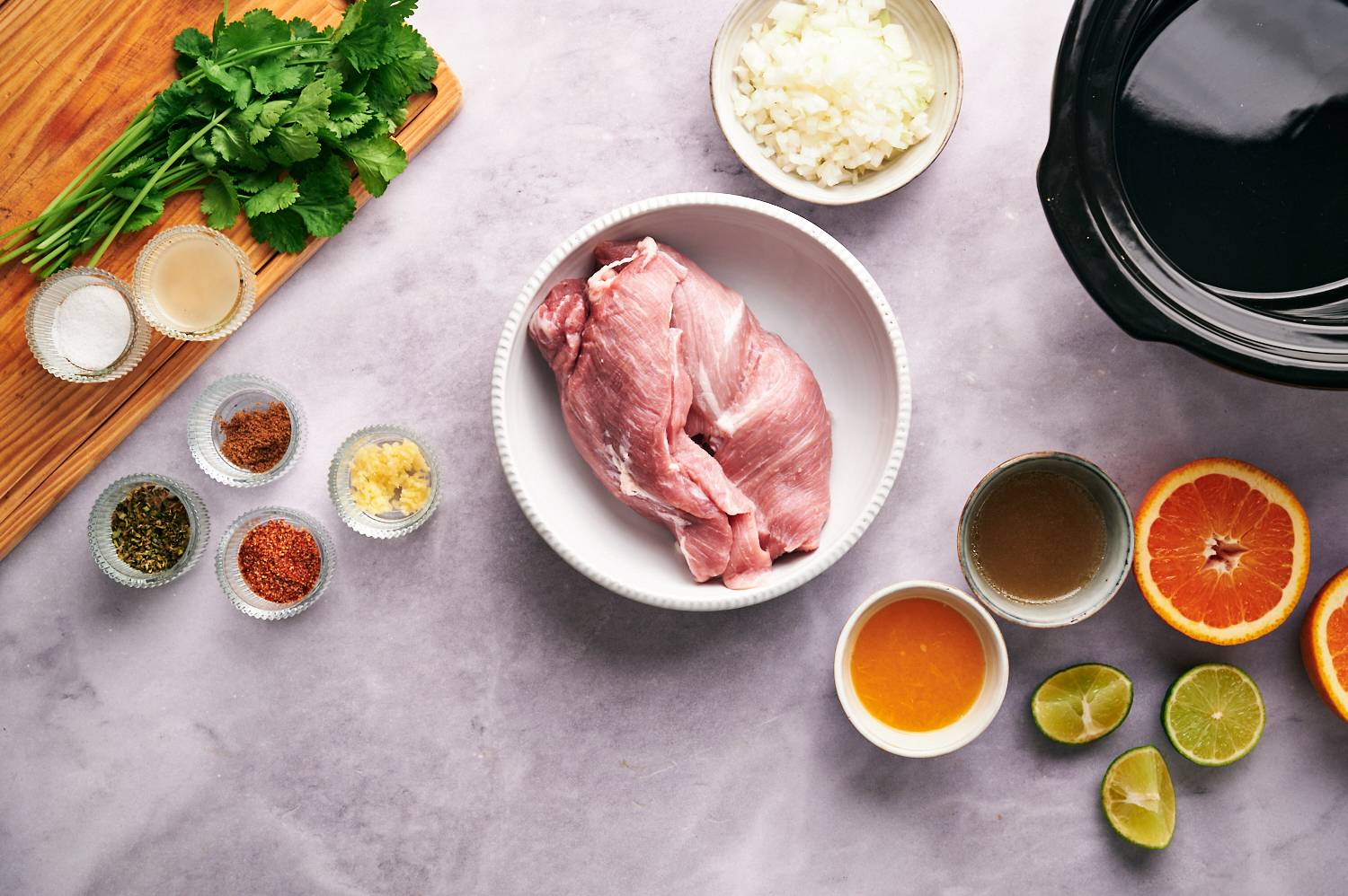 Ingredients for carnitas including pork shoulder, cilantro, spices, lime, and orange juice.