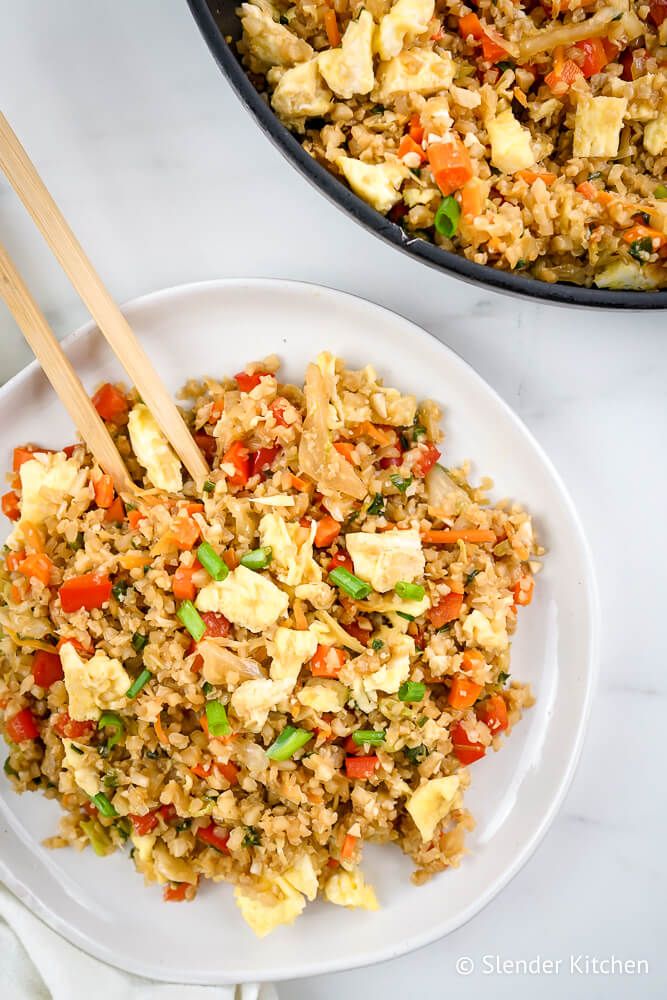 Fried cauliflower rice with vegetables and eggs on a plate with chopsticks.