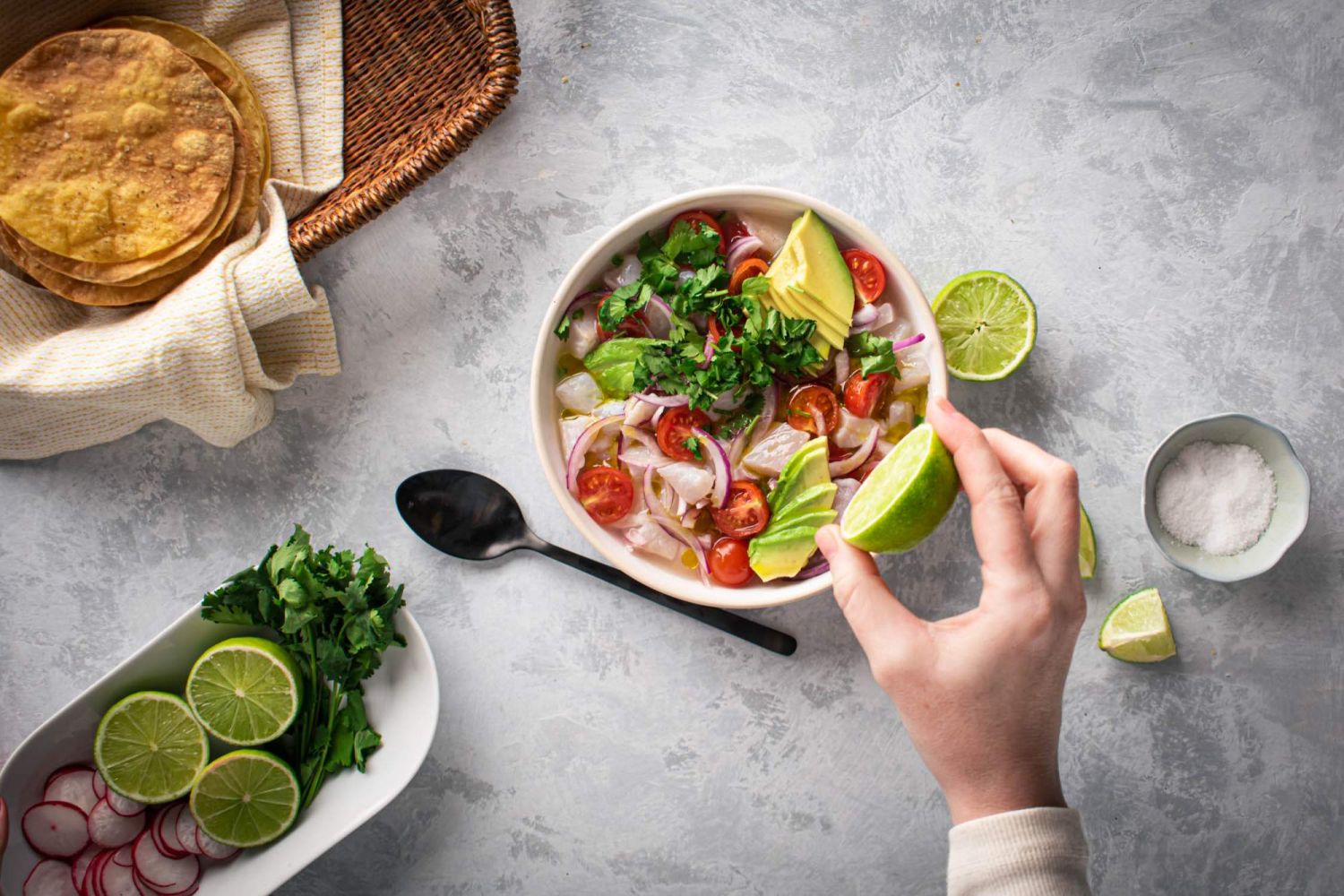 White fish ceviche cured in lime juice in a bowl with tomatoes, avocado, and red onion with baked tostadas and lime on the side.