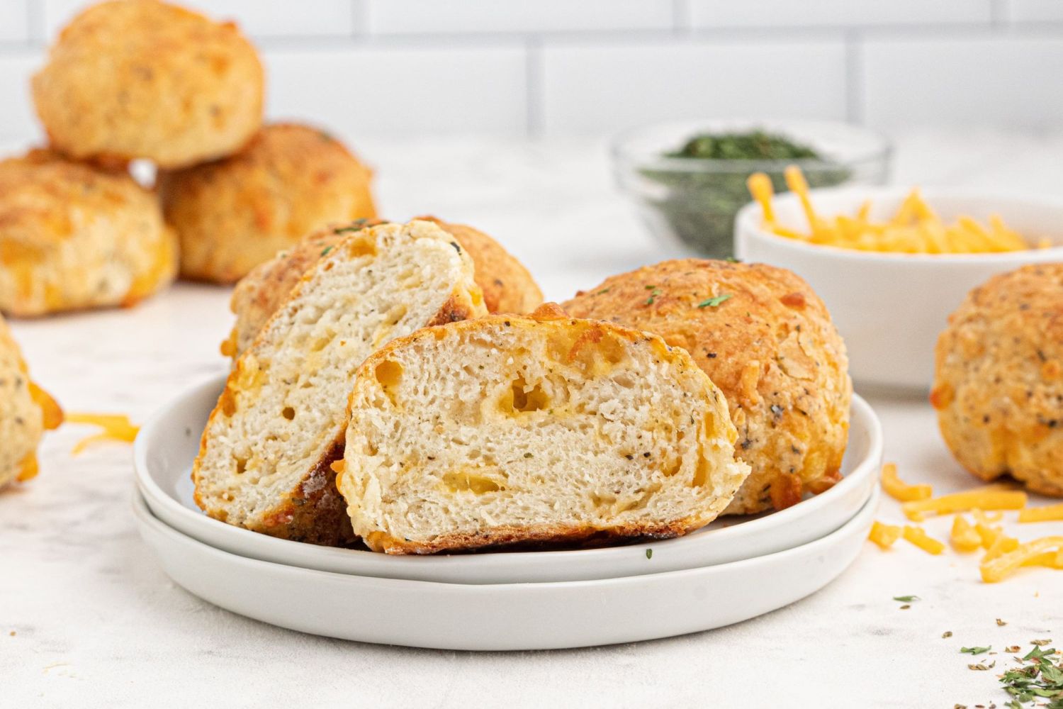 Two ingredient dough cheddar biscuits with shredded cheddar cheese and Italian seasoning cut in half on the plate.