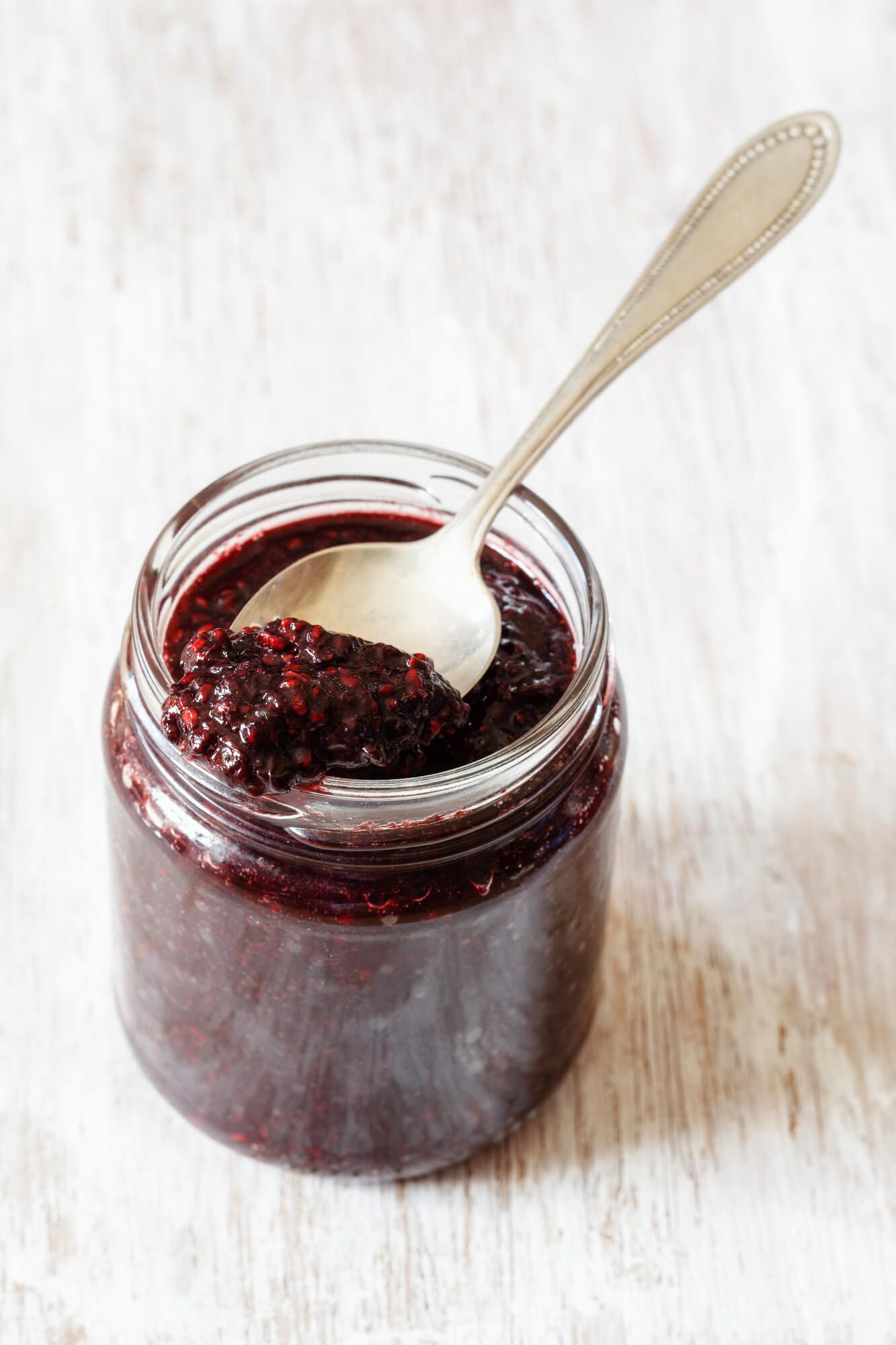Berry chia seed jam in a glass jar with a spoon and blackberry.