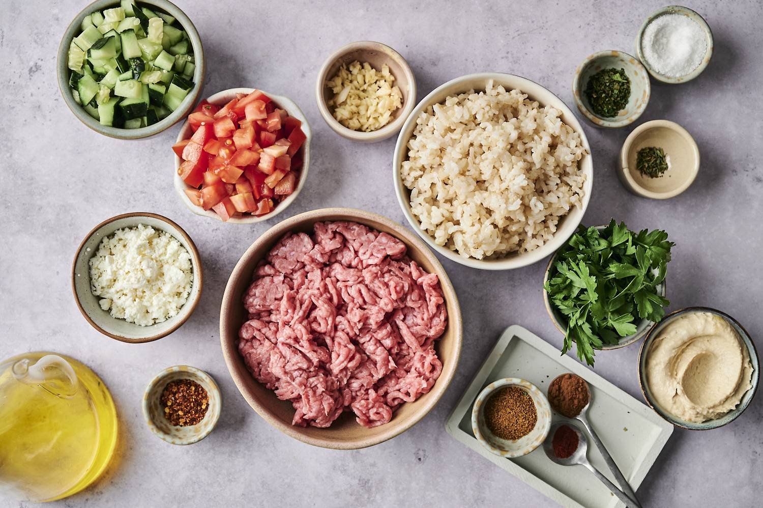 A variety of fresh ingredients, including ground meat, rice, vegetables, herbs and spices, are neatly arranged in the bowl.