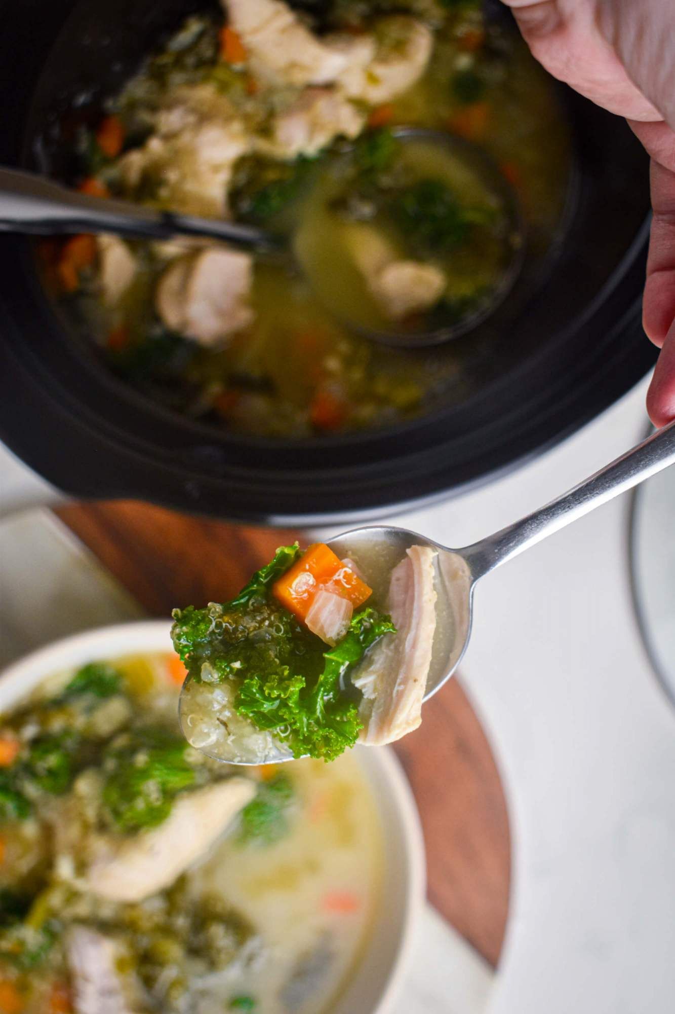 Crockpot quinoa and chicken soup with kale, carrots, celery, onion, and chicken broth in a bowl with a slow cooker.