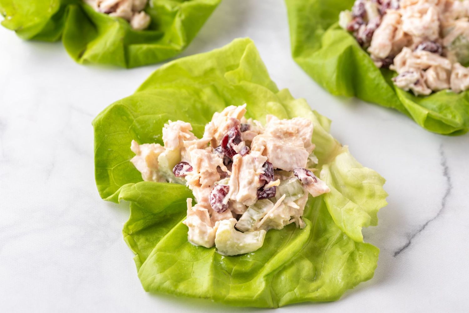 Lettuce wraps filled with chicken salad made with cooked chicken breast, celery, dried cranberries, and Greek yogurt.