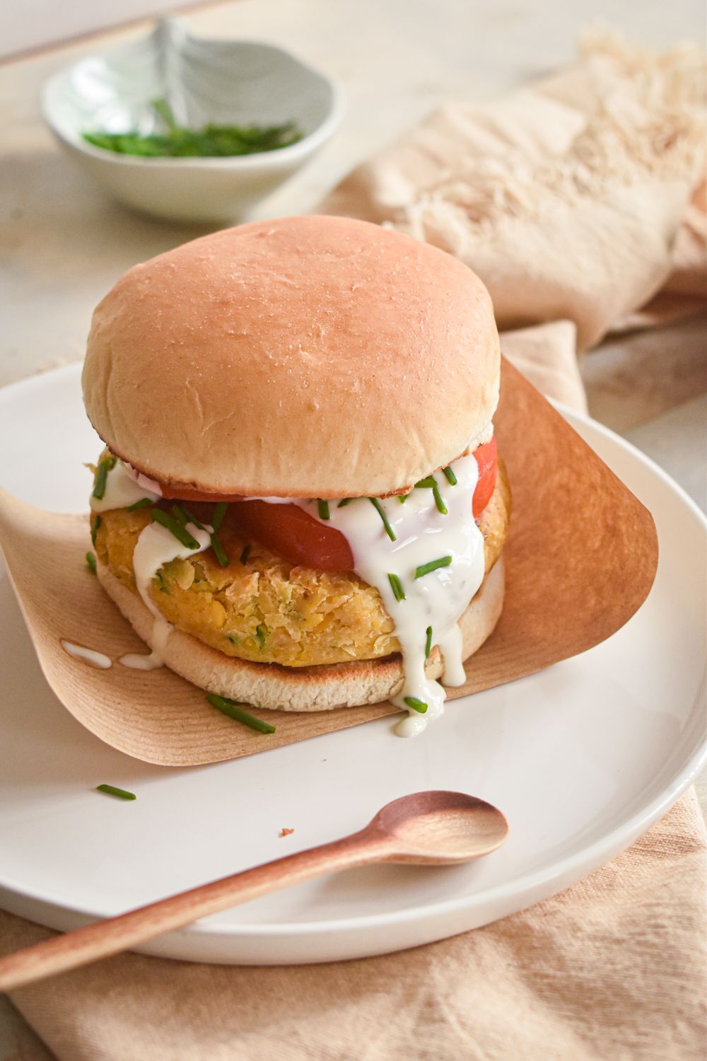Vegetarian chickpea burgers with ranch dressing on a white roll with tomatoes, lettuce, and drizzled ranch dressing.