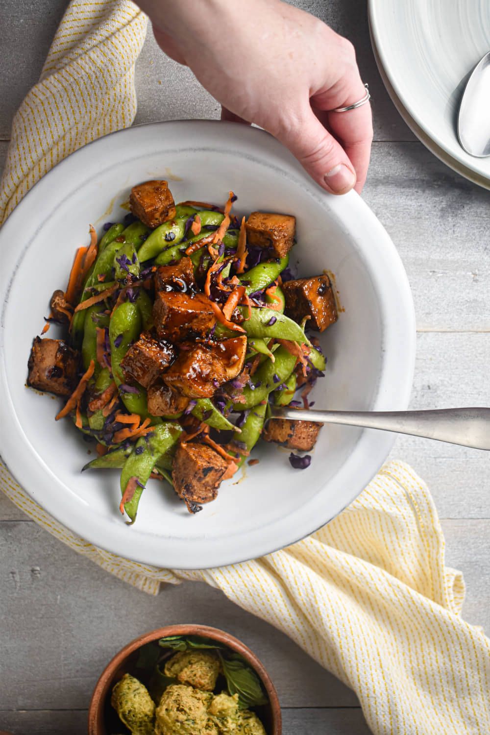 Crispy tofu with Asian stir fry sauce, sugar snap peas, carrots, and cabbage in a bowl.