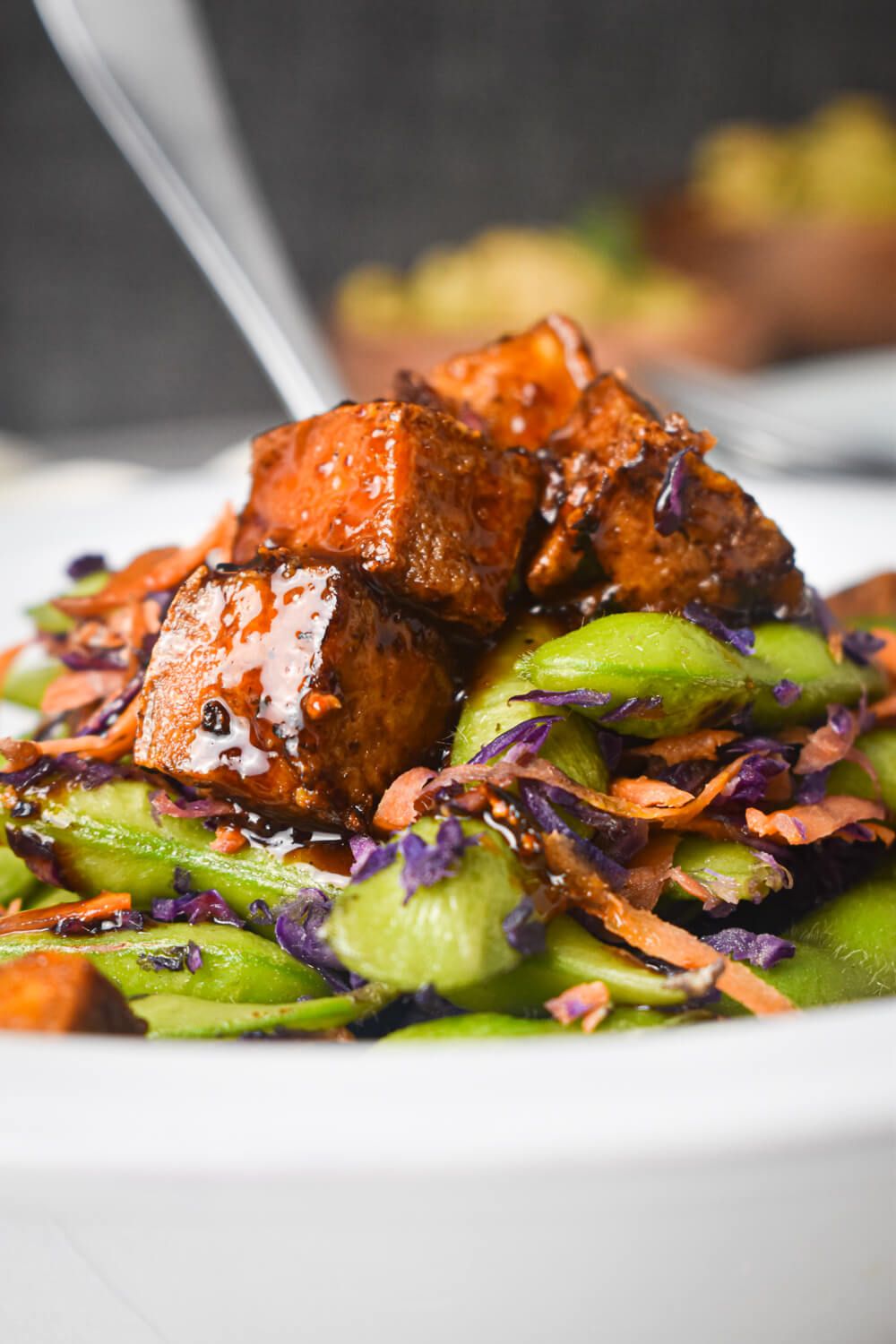 Chili glazed tofu with sugar snap peas, carrots, cabbage, and crispy tofu in a bowl with a fork.