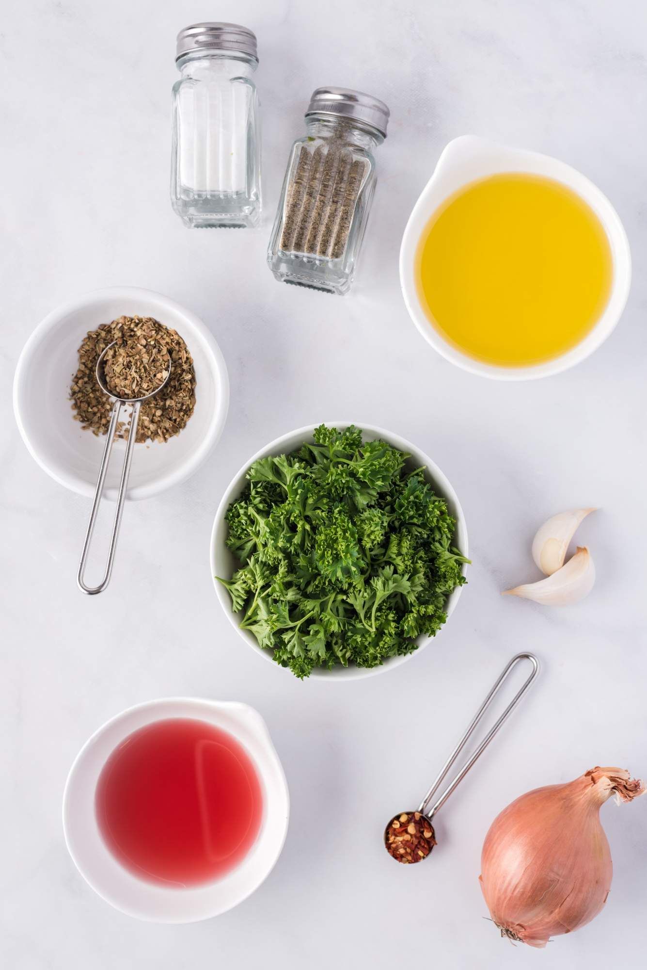 Ingredients for chimichurri including parsley, olive oil, garlic, shallot, red wine vinegar, and red pepper flakes.