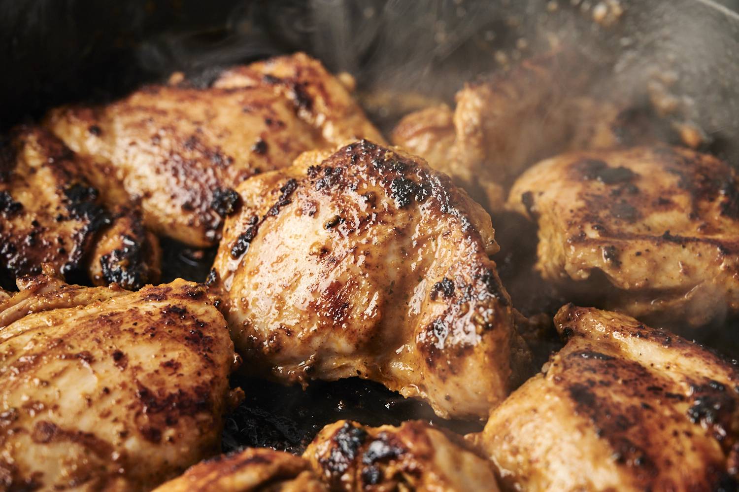 Juicy chip chicken thighs scallops scalded in a hot frying pan with golden crust and smoky char marks that release a delicious steam.